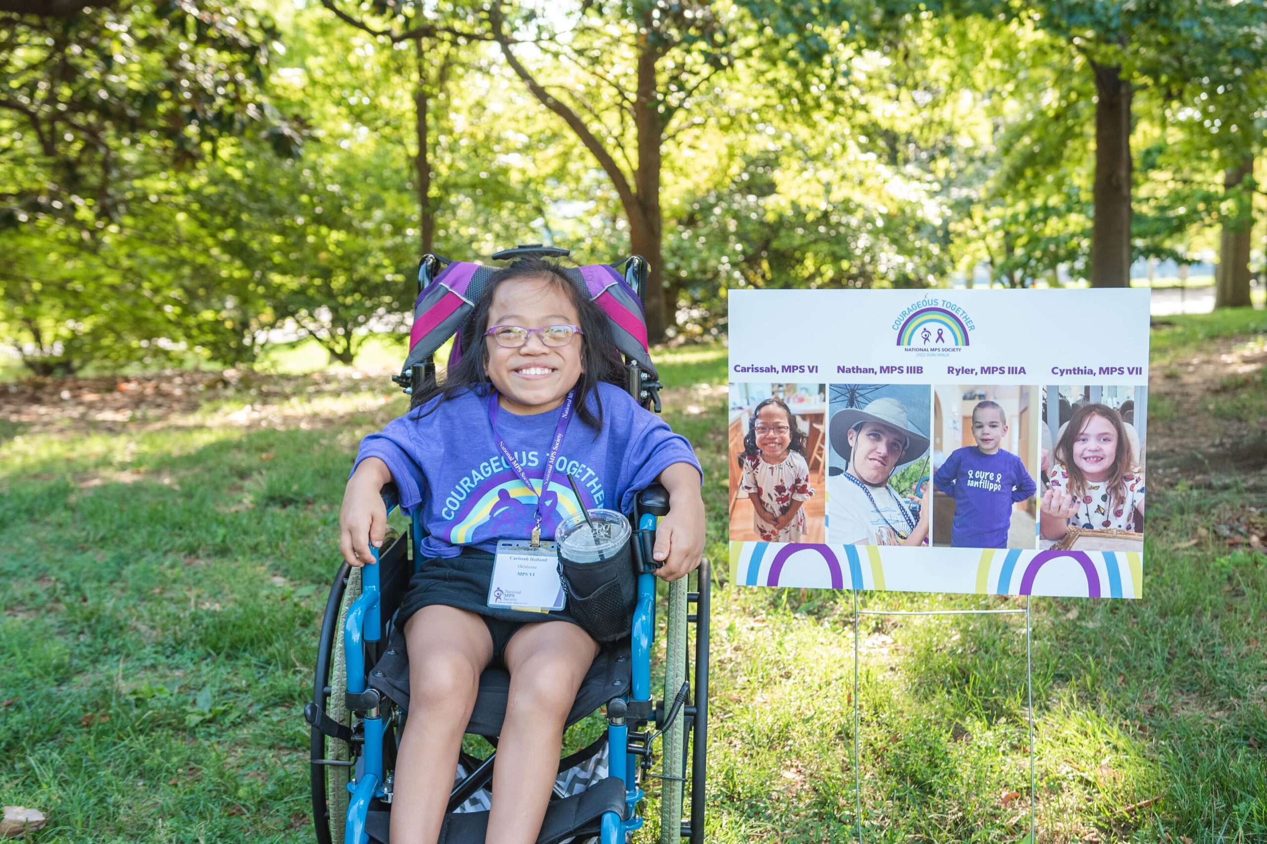 Smiling girl in a wheelchair next to an MPS awareness banner