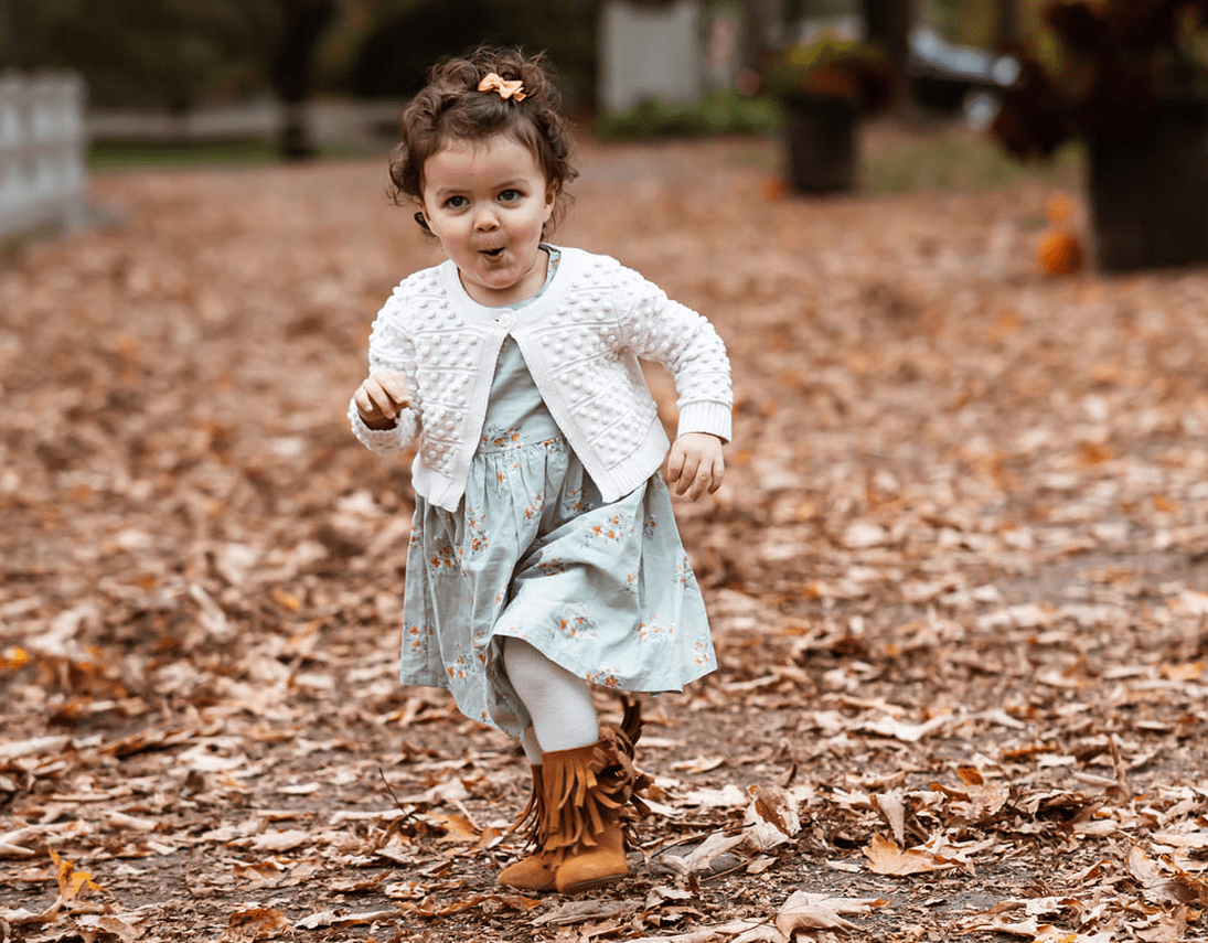 Small girl in a white sweater running through fall leaves