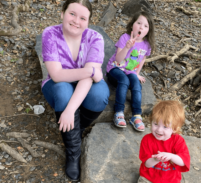 Three children sit on a rock in the park