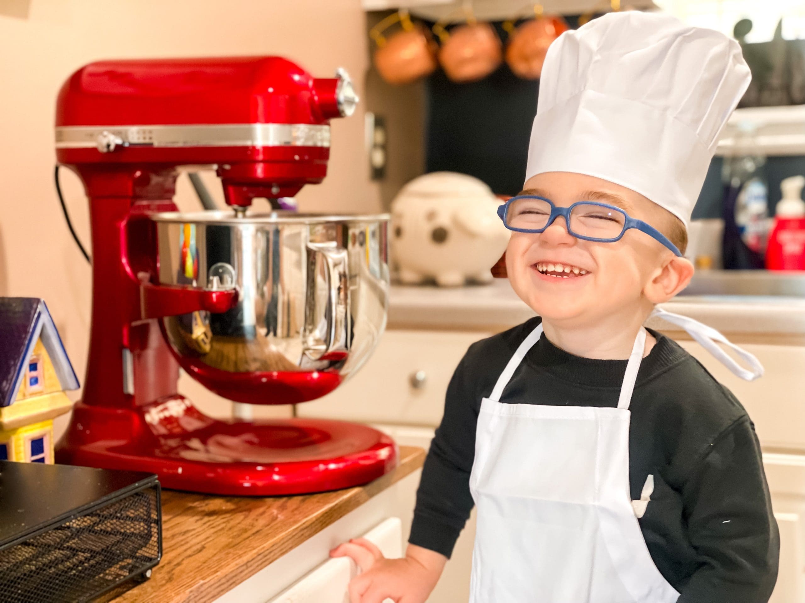 Boy in chefs hat and apron in the kitchen with a red mixer