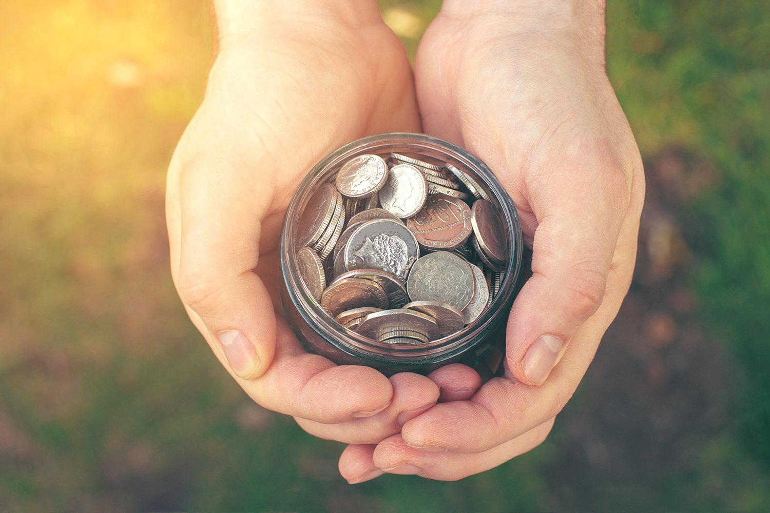 Soft sunlight shining on a pair of hands holding a jar full of change.