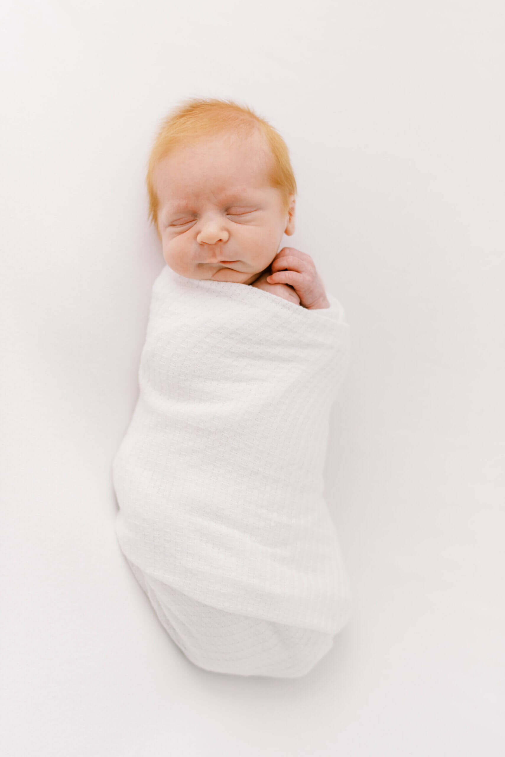 Baby swaddled in a white blanket, eyes closed